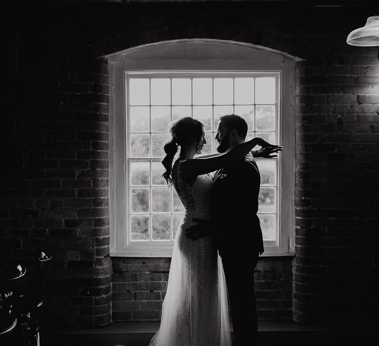 Black and white couple portrait of bride and groom posing in front of a window 