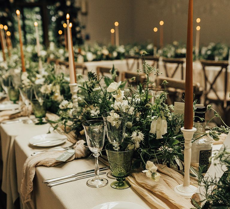 Neutral tone taper wedding candles with white tablecloths and white flowers and foliage table runner for green wedding theme 