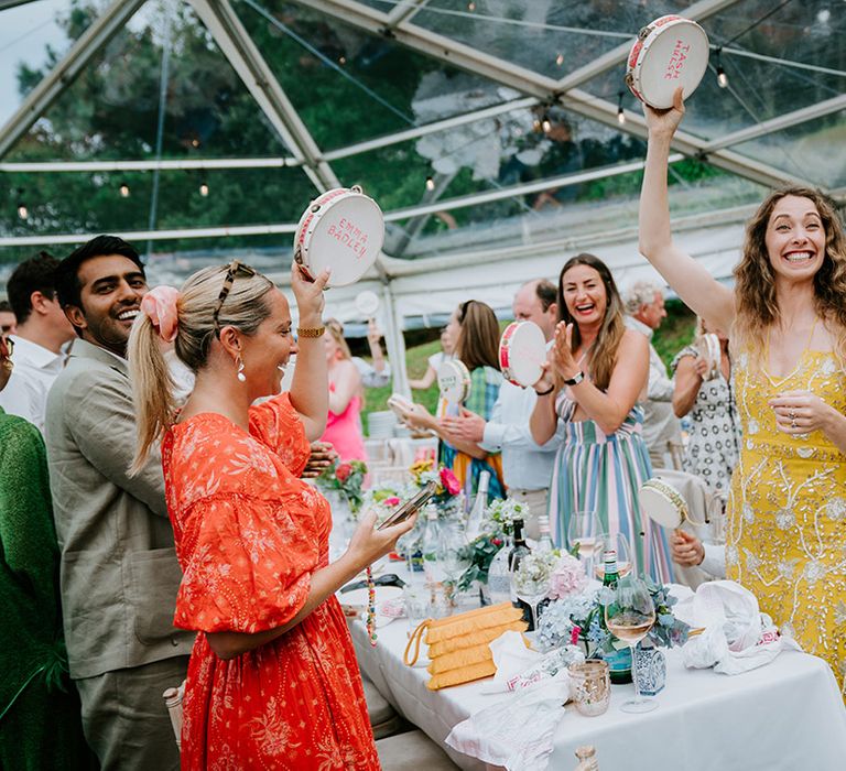 Wedding guests wave tambourines in greetigto bride and groom entering wedding breakfast 