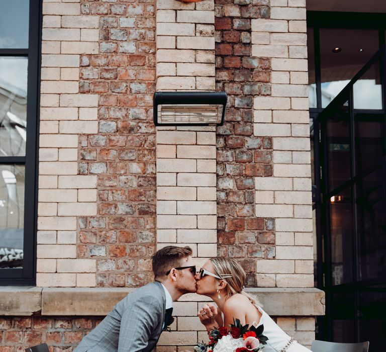 Bride in a Massimo Dutti jumpsuit kissing her groom across the table 