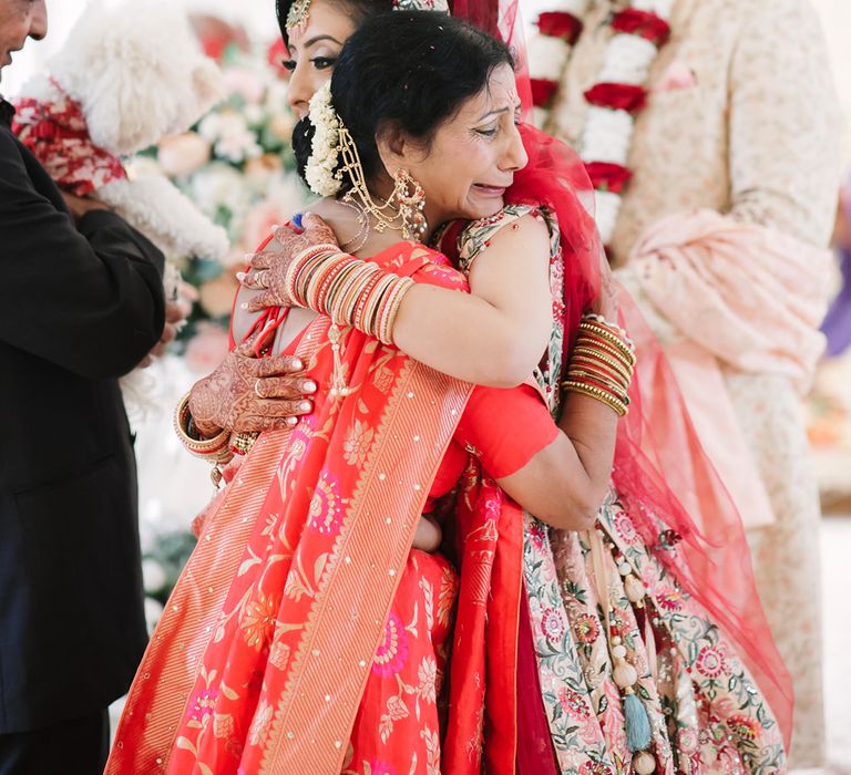 Emotional mother of the bride hugging her daughter at her vidaai ceremony during the Hindu wedding 