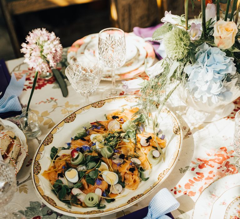 Dish of smoked salmon and boiled egg with edible flowers on rose tablecloth with purple menus and blue gingham ribbons