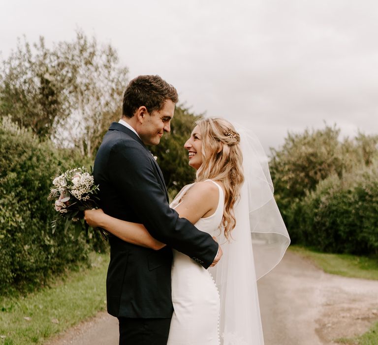 Bride and groom embracing in a country lane at rural wedding 