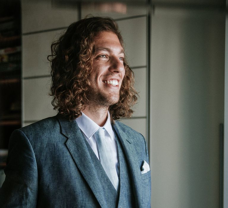 Groom in a navy blue, light linen destination wedding suit with shoulder length naturally curly hair 