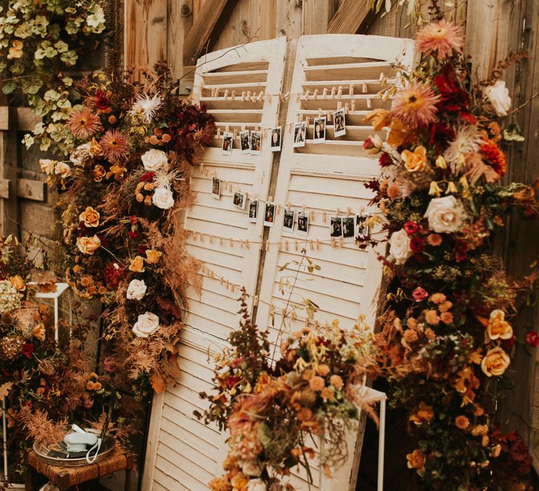 Autumn themed wedding decor with Wooden shutter polaroid picture display decorated with orange and red flowers 