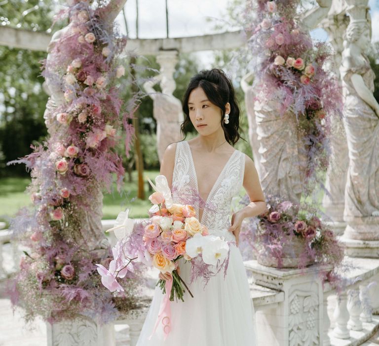 Dark haired Asian bride holds floral bouquet filled with pastel coloured flowers