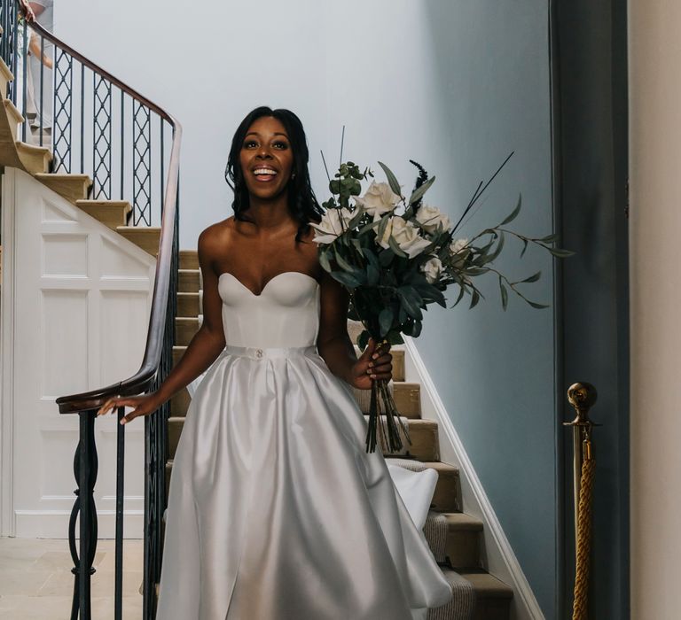 A Black bride walks down the stairs in a strapless wedding dress. 