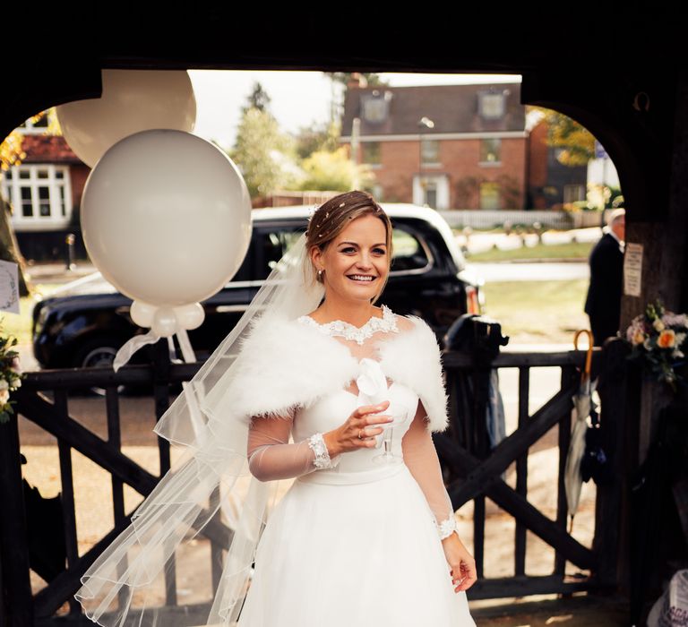 Bride stands smiling whilst holding champagne with confetti in her hair