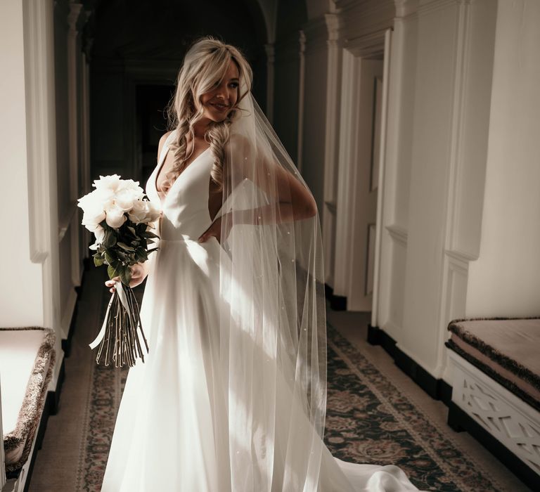 Bride wears Suzanne Neville gown and holds long stemmed white bouquet