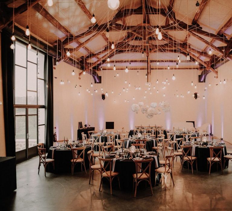 Round wedding tables with black tablecloths, hanging lights and a hanging cloud installation