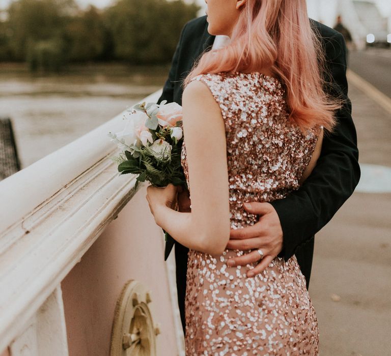 Bride in sparkly pink dress with pink hair looking over the Albert Bridge in Chelsea with her groom. 