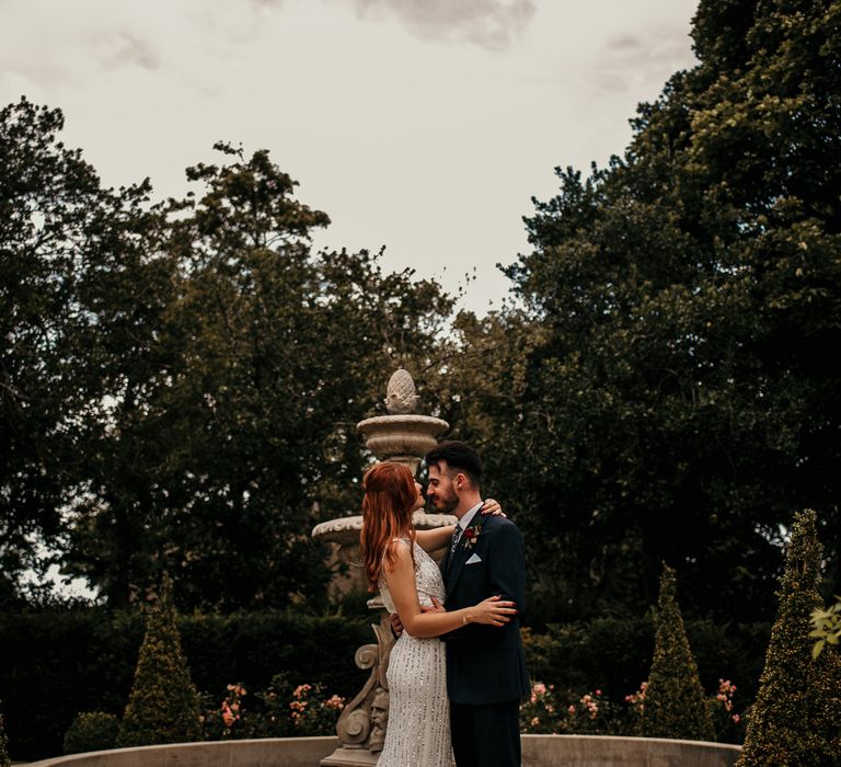 Bride & groom stand in front of fountain and kiss on their wedding day