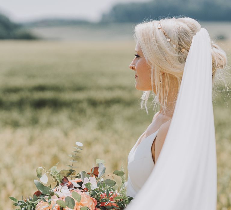 Bride wears veil as it blows in the wind and carries pastel bouquet