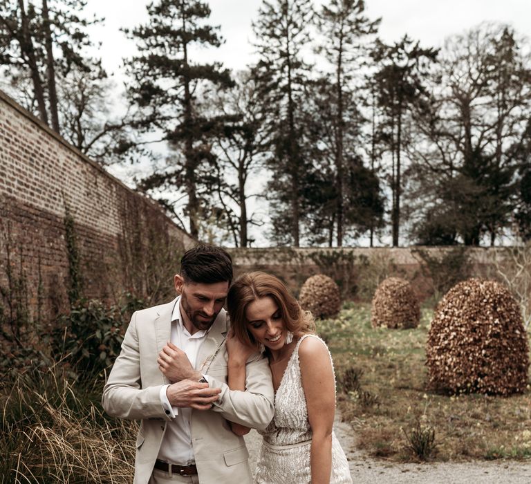 Intimate bride and groom portrait with groom in a beige suit and bride in a stylish wedding dress with straps 