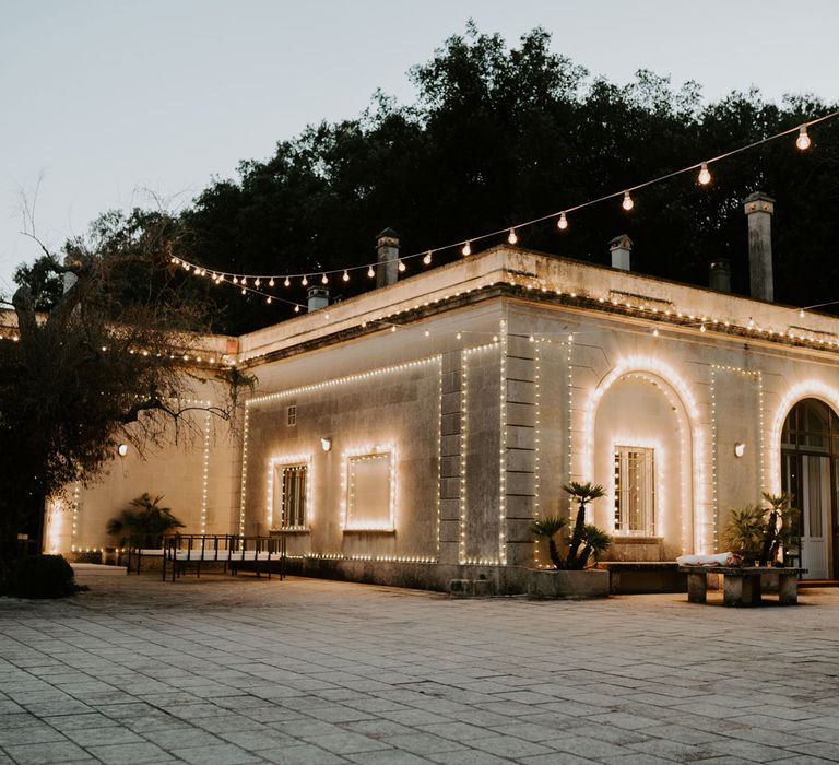 One story stone block buying with low windows and archways covered in fairy lights in stone courtyard covered in fairy lights at Tenuta Tresca, Puglia, Italy