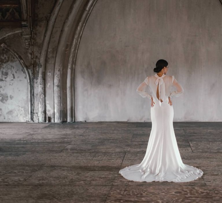 Bride stands in grey room as her bridal gown is spread out around her