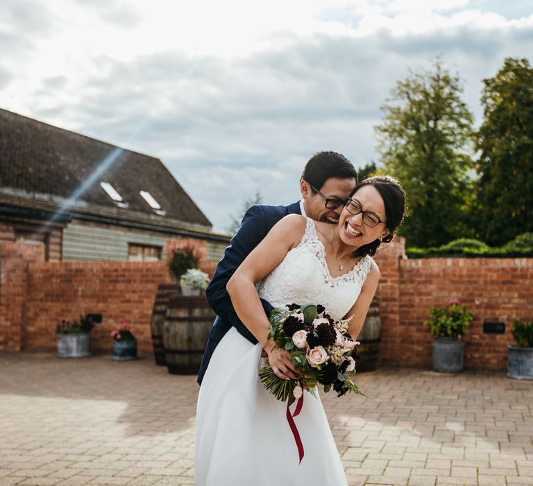 Bride & groom laugh together and embrace outdoors on wedding day