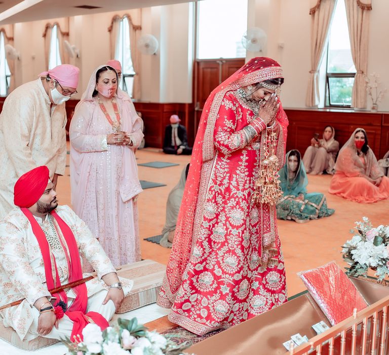 Bride prays during Sikh wedding ceremony as her groom looks up toward her