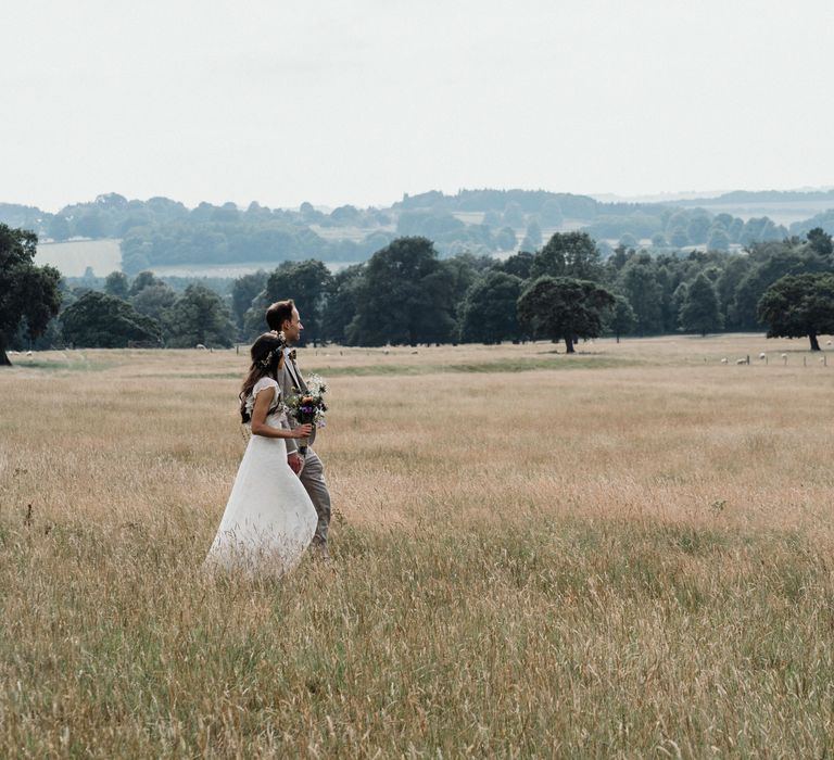 Bride & groom walk across field with one another on their wedding day