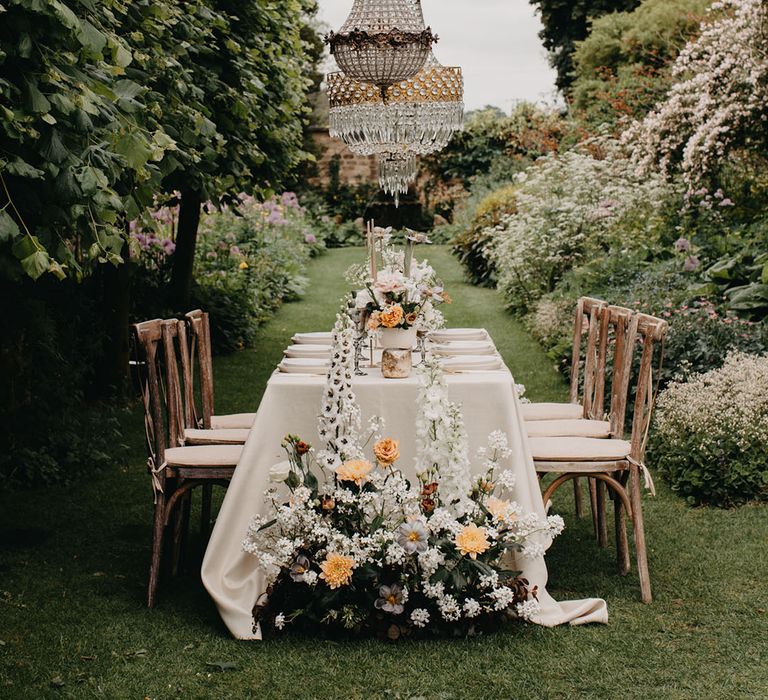 Elegant garden wedding reception with white and peach wedding flowers and chandelier light installation