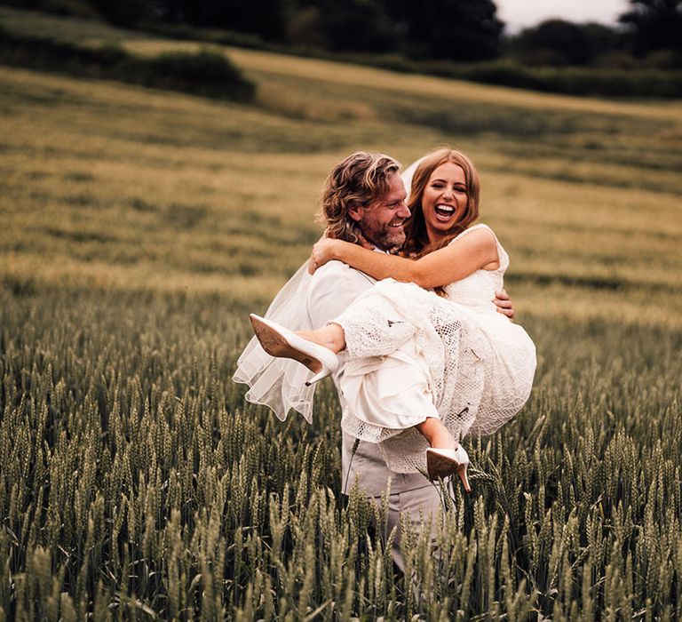 Groom carries bride through fields