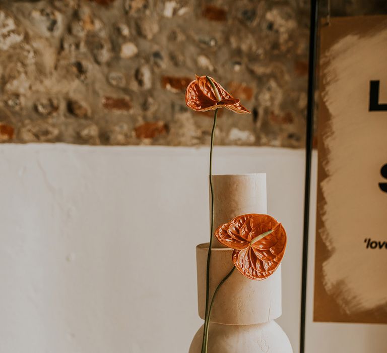 Tall marble wedding cake on a gold cake stand decorated with orange anthurium flower stems 