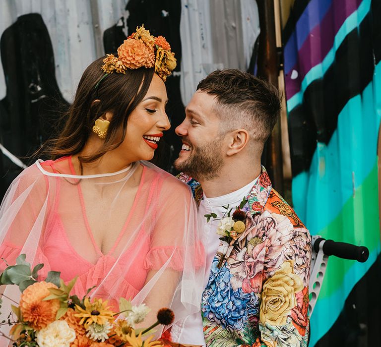 Portrait of the bride in a coral wedding dress and Frida Kahlo inspired flower crown with her groom in colourful patterned jacket