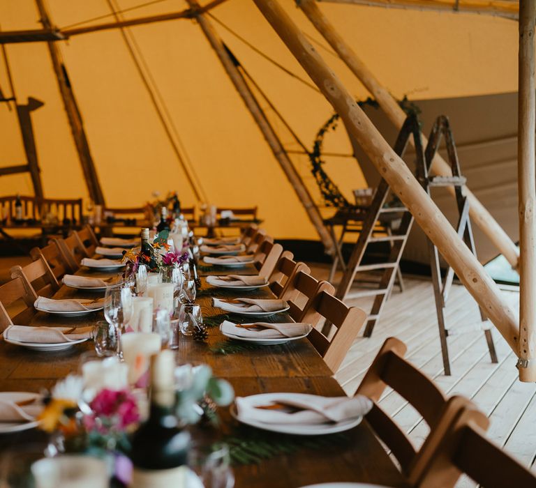 Interior of tipi at Wellington Wood Norfolk with long wooden table, florals, candles and place settings for late summer wedding