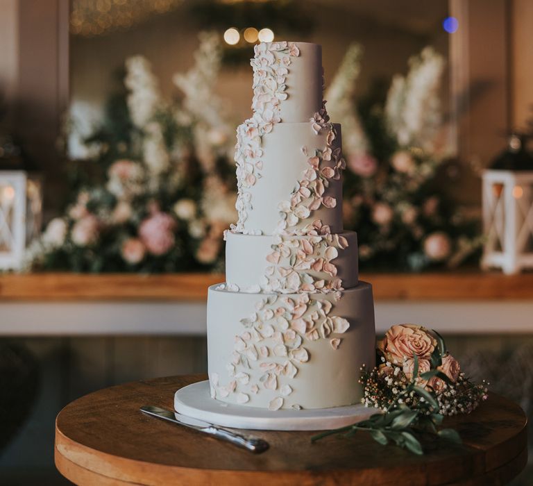 Four tier pale blue wedding cake with petal icing detailing on round wooden table for summer wedding at Primrose Hill Barn