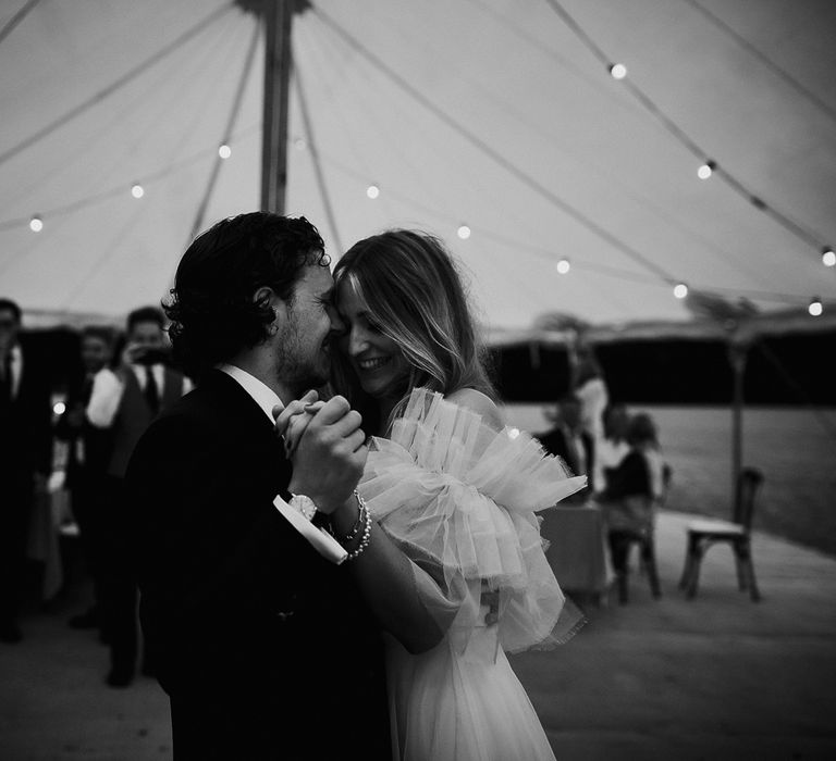 Bride in white Halfpenny London Mayfair dress with ruffle sleeves dances with groom in suit during marquee garden wedding reception in Cornwall