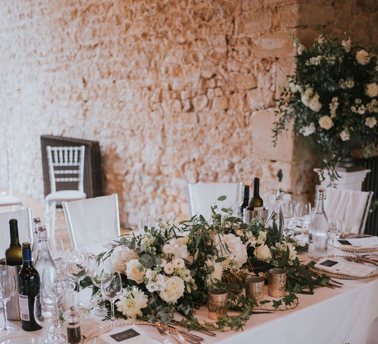 White and green floral centrepiece on white tables with gold tableware for Notley Abbey wedding reception