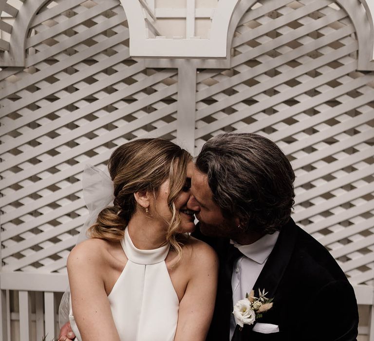 Groom in a black suit kissing his bride in a halterneck wedding dress 