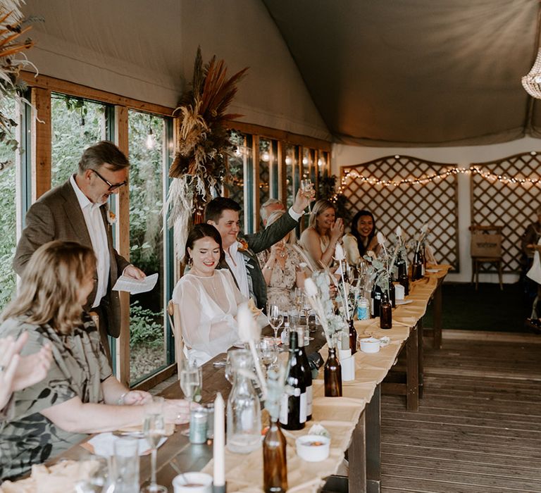 Father of the bride wedding speech with dried orange flower displays behind the top table 