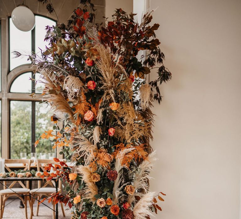 Large mixed floral column with orange and green florals and pampas grass with silver disco balls and candles for intimate wedding ceremony