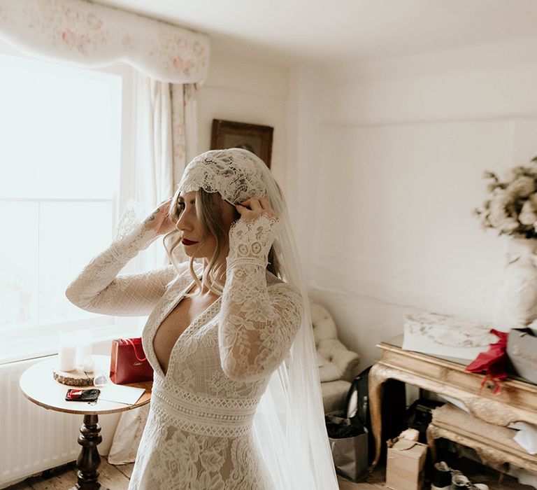 Bride in a long sleeve wedding dress with bell sleeves putting on her Juliet cap veil 