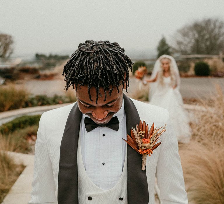 Groom in white tuxedo with orange buttonhole