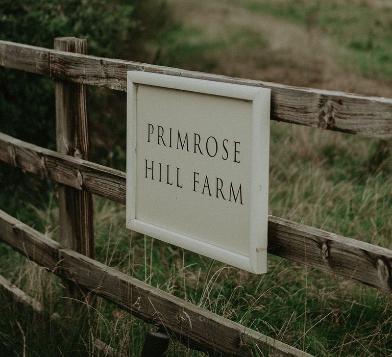 White sign saying 'Primrose Hill Farm' with wooden gate entrance to contemporary barn venue