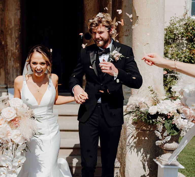 Confetti moment at Elmore Court with bride in a fishtail wedding dress holding a white bouquet with orchids, roses, astilbe and pampas grass and her grooms hand in a tuxedo 