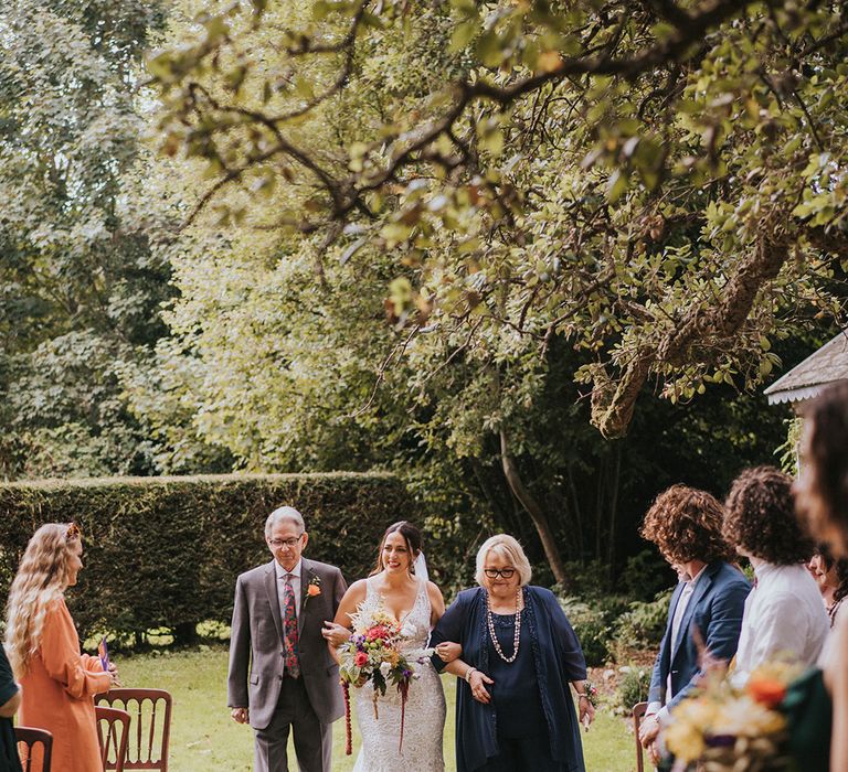 Bride in Made With Love Bridal wedding dress is walked down the aisle by her parents for outdoor wedding