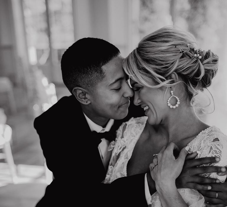 LGBTQI+ couple embracing at Hodscok Priory with bride in a lace wedding dress with pinned up with pearl slides 