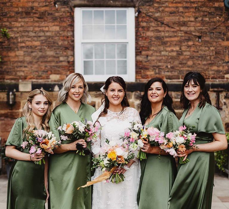 Bridesmaids in green satin wrap bridesmaid dresses and gold sandals with a block heel with bride in high neck long sleeve lace wedding dress