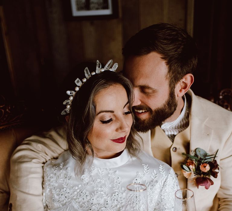 Groom in a beige suit embracing his bride in a satin wedding dress with embroidered and fringe design