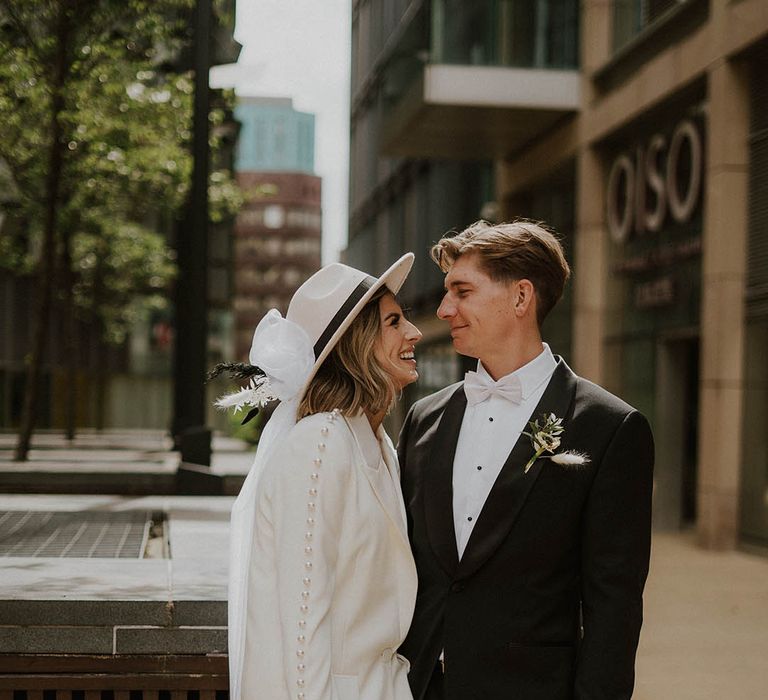 Bride and groom smile and look into each other's eyes with bride in Nadine Merabi pearl suit and groom in black tie 