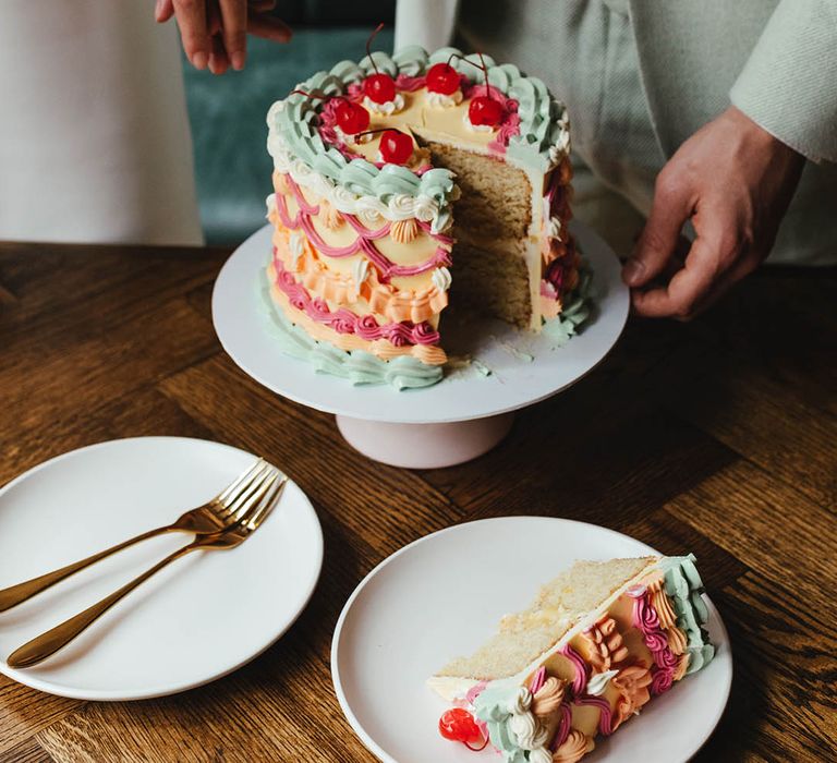 Sponge wedding cake with colourful buttercream retro design and cherries on a white cake stand 