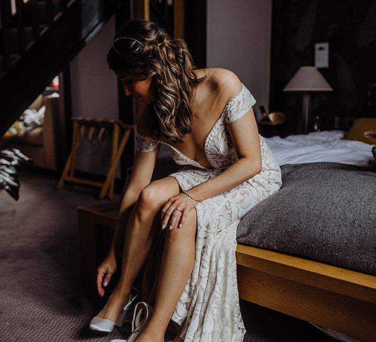 Bride in lace wedding dress putting on her white wedding heels 