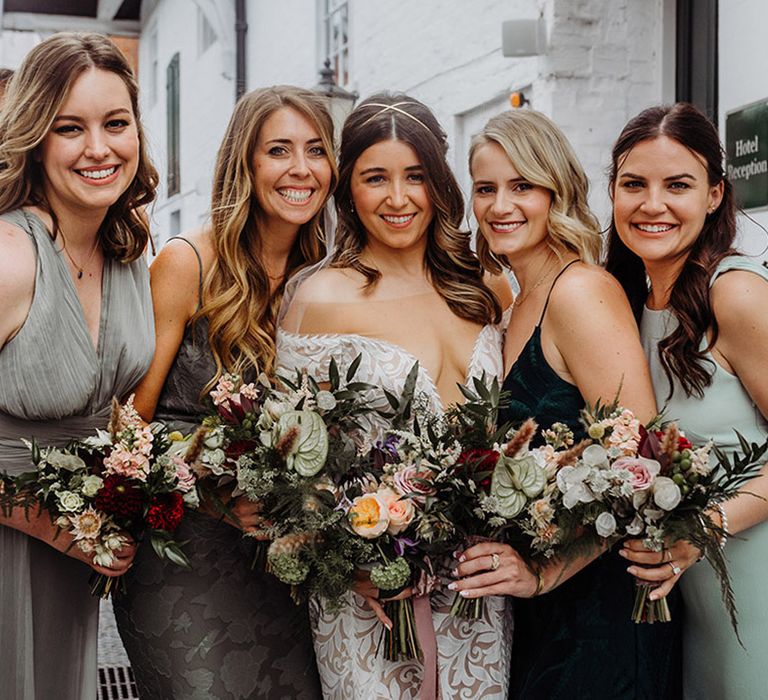 Bride with bridesmaids in a variety of shades of green and bride in a boho style wedding look with gold headband and fitted lace dress