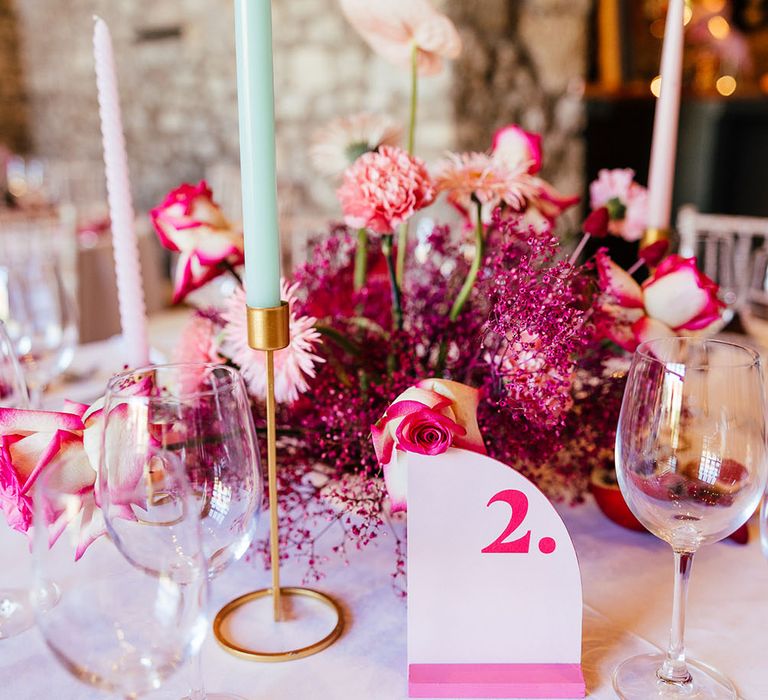 Bright pink floral centrepiece surrounded by pastel candles and dried fruit decor for modern tablescape 