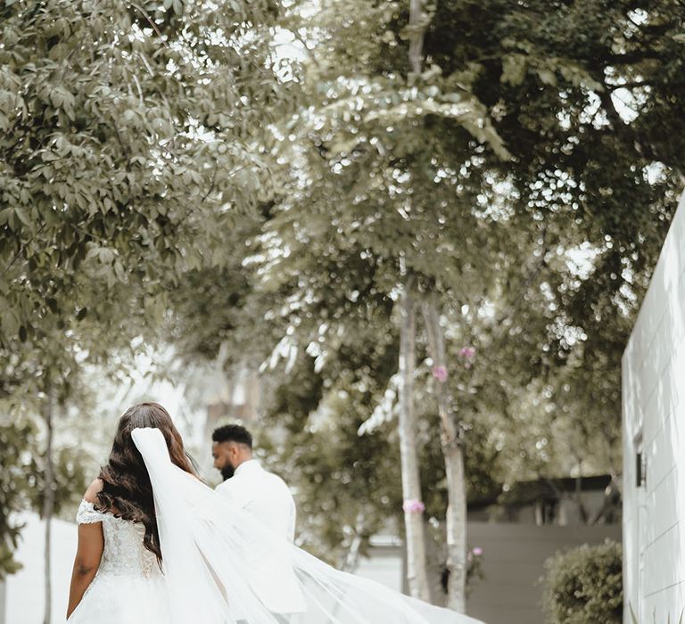 Bride wears floor-length veil as it blows behind her as she walks alongside her groom after first-look moment 