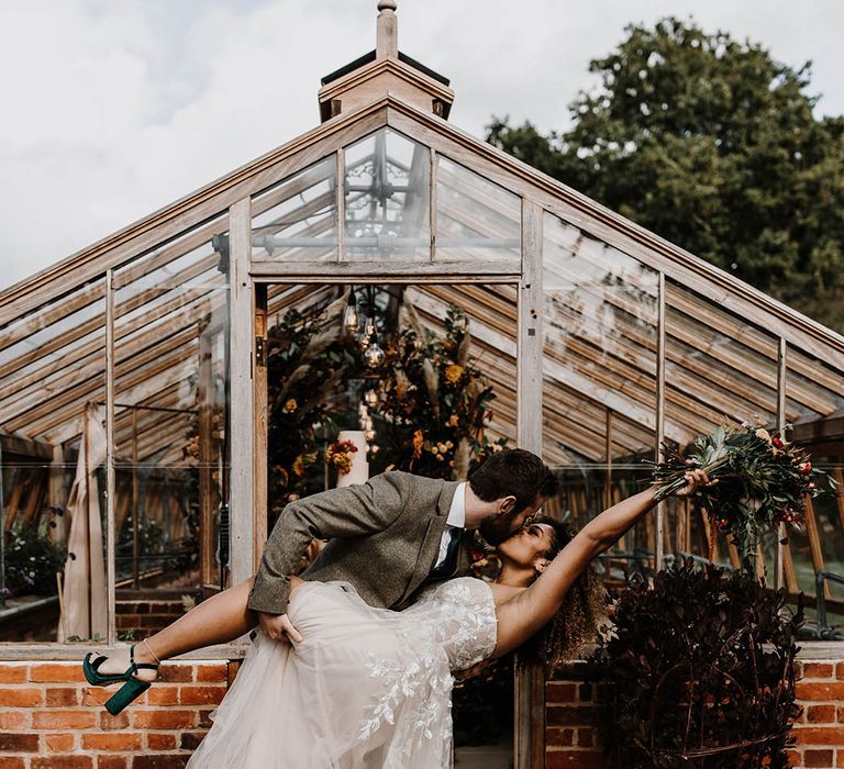 Groom in a three piece grey suit leans the bride back in a kiss who wears green velvet platform wedding shoes and a sparkly corset wedding dress