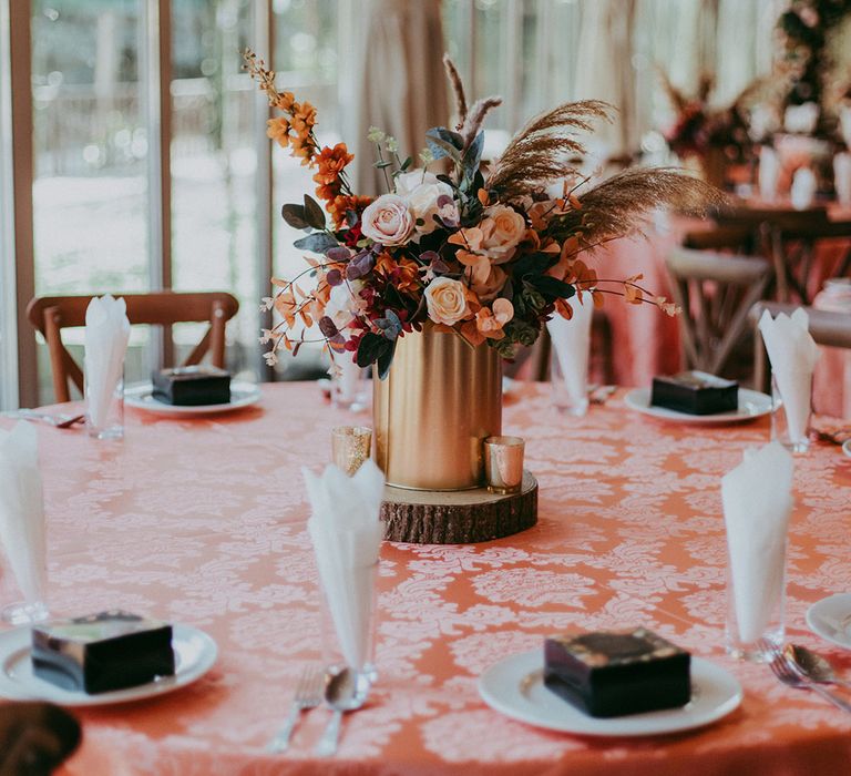 Autumnal styled floral centrepiece in brass vase on circular tree block